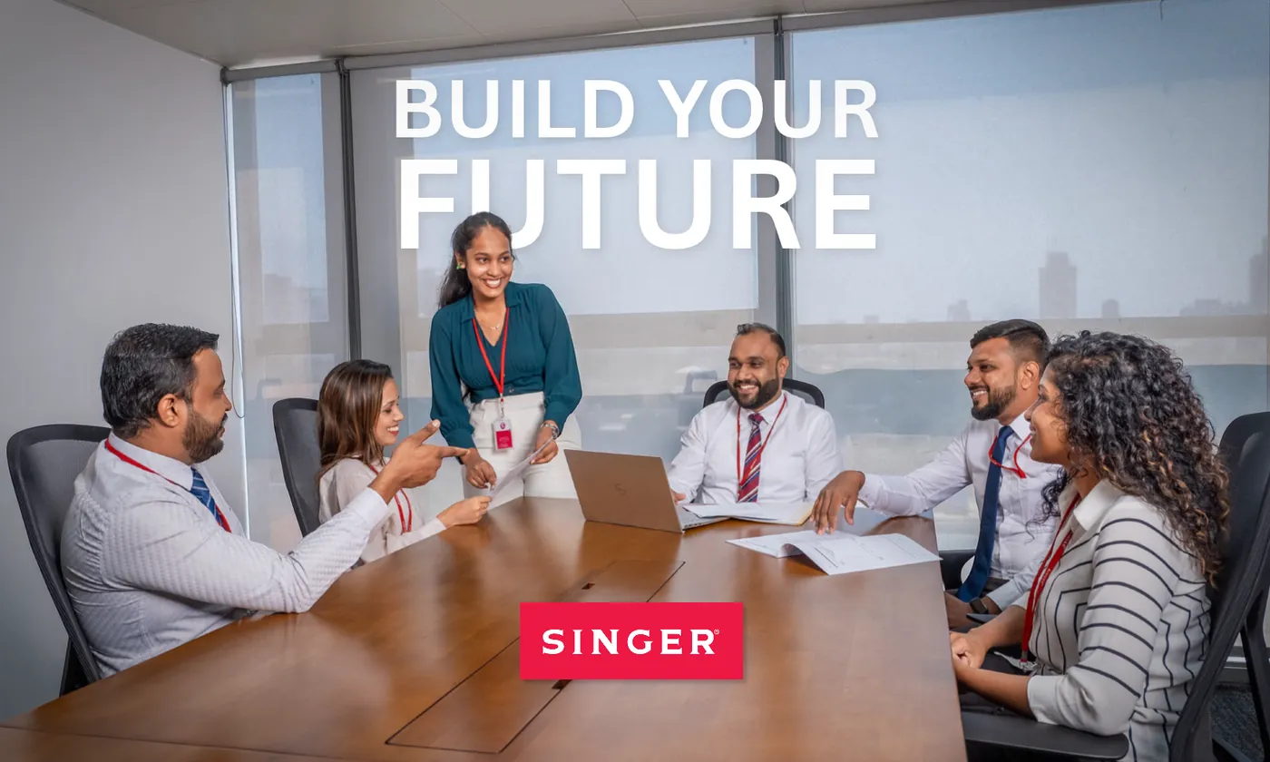 Six Singer colleagues laughing together around a boardroom table beneath the words “Build Your Future”.