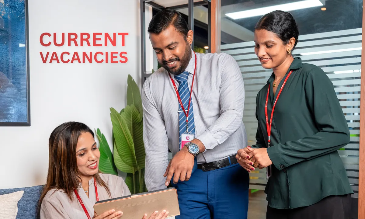 Three Singer employees reviewing a tablet together beneath the words “Current Vacancies”.